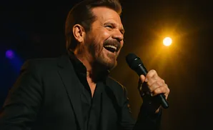 Singer with a beard and black suit holding a microphone and singing on stage.