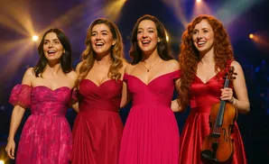Four women in elegant red dresses smiling on stage. One holds a violin.