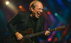 A man in a suit plays an electric guitar with his eyes closed and mouth open in excitement.
