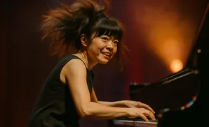 A woman with her hair flying plays a piano with her hands on the keys.