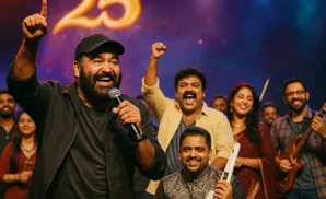 Man in a black cap and jacket holds a microphone and points up, celebrating with a diverse group of people.