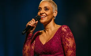 Singer with short blonde hair wearing a sparkly maroon dress and holding a microphone.