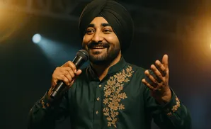 Man in a dark green, embroidered kurta and black turban smiles and speaks into a microphone.