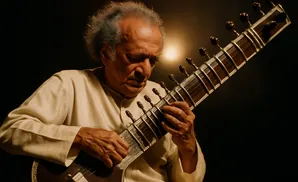 An older man with gray hair plays the sitar.