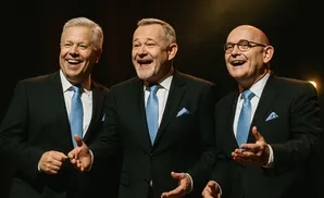 Three men in suits and ties, laughing on stage.