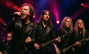 A male singer in a black leather jacket and four male guitarists perform on a dimly lit stage with purple and red spotlights.