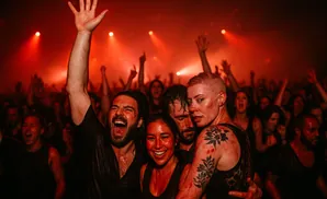 People in a dark, red-lit room, all covered in what appears to be red paint, are joyfully dancing and screaming.