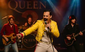 A Queen tribute band performs on stage with the lead singer in a yellow jacket and a guitarist on the right.
