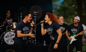 A band performing on stage, with two lead singers, a guitarist, and a drummer.