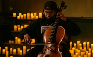 A Black cellist plays in front of many lit candles.