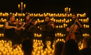 A string quartet performs for an audience amidst a backdrop of flickering candles.