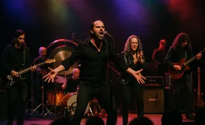 A band performs on stage, with singers and guitarists in black clothing.