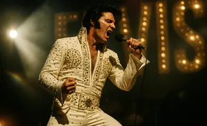 Elvis Presley in a sequined jumpsuit sings into a microphone, with illuminated 