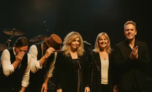 A band of five musicians bows on stage, with two men in the foreground covering their faces.