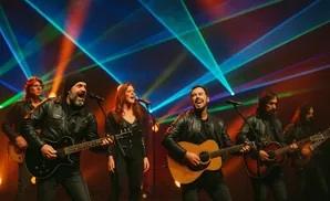 A band performs on stage with colorful laser lights projected behind them.
