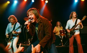 A band performs on stage with a singer in the foreground and other musicians playing guitar and drums.