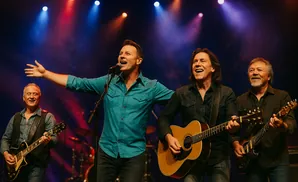 Country band performs on stage with guitars and microphones under colorful stage lights.