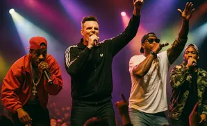 Four rappers perform on stage with colorful spotlights and a cheering crowd in the background.
