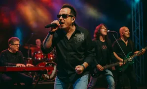 A rock band performs on stage, with the lead singer in sunglasses holding a microphone.