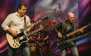 A band performs on stage, with two guitarists in the foreground and a drummer in the background.