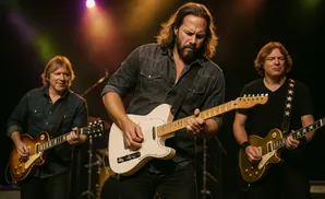 Three men playing guitars on stage with stage lighting.