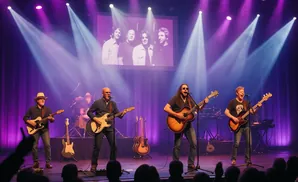 A band performs live on stage under purple and white spotlights, with a projected image of four men behind them.