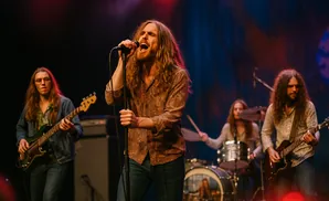 A rock band performs on stage, with the lead singer in the foreground singing into a microphone.