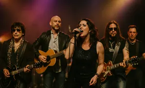 A band of five musicians performing on stage with a female singer in the foreground.