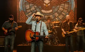 A band performs country music on stage, with a lead singer playing guitar and wearing a cowboy hat.