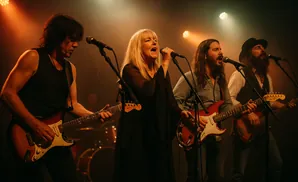 A woman sings into a microphone while a band performs on stage.