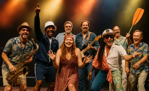 A band of seven people smiling and posing on stage, some holding instruments and a paddle.