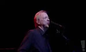 boz scaggs singing on stage under dim colored lighting.