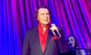 engelbert humperdinck singing on stage in a black and red suit.