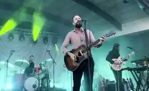 father john misty singing on stage while playing the guitar