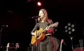 gracie abrams singing on stage while playing the guitar.
