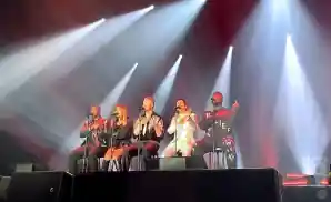 pentatonix performing on stage sitting in chairs.