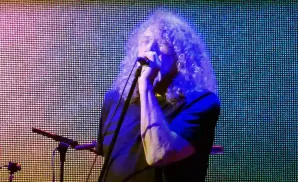robert plant performing on stage under multi-colored lighting.