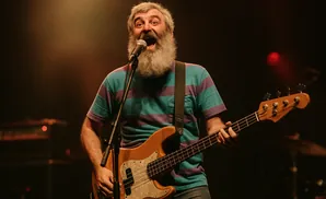 Man with a long beard singing and playing a bass guitar on stage.