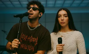A man and woman singing into microphones in front of a blue background.