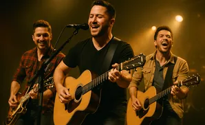 Three men playing guitars and singing on stage with warm lighting.