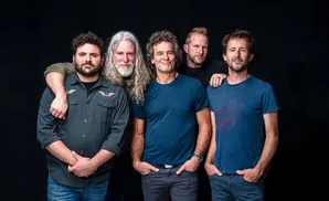 Five men in casual clothing pose for a photo in front of a black backdrop.