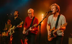 A band performs on a dimly lit stage with warm stage lighting.
