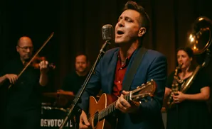 A male singer in a blue suit sings into a vintage microphone while playing an acoustic guitar.