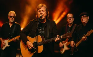 A band performs on stage with the lead singer playing an acoustic guitar and singing into a microphone.