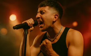 A male singer belts into a microphone, eyes closed, with a fist clenched.