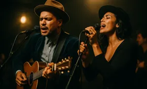 A man and woman singing into microphones and playing guitar.
