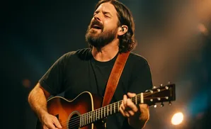 Man singing with his eyes closed while playing an acoustic guitar on stage.