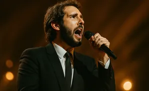 A man in a black suit sings into a microphone, his mouth open in song.