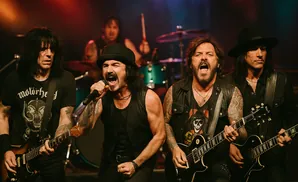 A rock band performs on stage with singers and guitarists in black.