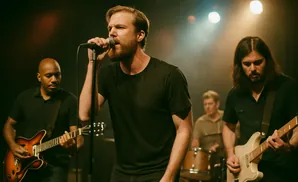 A band performs on stage with a lead singer in front and guitarists and drummer behind.